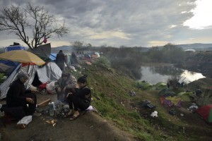 People sit in a makeshift camp at the Greek-Macedonian border, on March 12, 2016, near the Greek village of Idomeni, where thousands of refugees and migrants are stranded by the Balkan border blockade. More than 14,000 mainly Syrian and Iraqi refugees including many children are camped out at the squalid camp where they have been stranded by Skopje's decision to close the frontier. Days of heavy rain have turned Greece's Idomeni border camp into a foul-smelling bog, exposing migrant children to raw sewage, noxious fumes and bitter cold, with aid workers describing conditions as "critical". / AFP / DANIEL MIHAILESCU