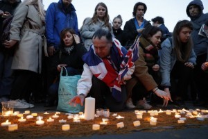 People including a man draped in the Union Flag, John Loughrey (C), light candles on a patch of sand during a vigil in Trafalgar Square in central London on March 23, 2017 in solidarity with the victims of the March 22 terror attack at the British parliament and on Westminster Bridge.  Britain's parliament reopened on Thursday with a minute's silence in a gesture of defiance a day after an attacker sowed terror in the heart of Westminster, killing three people before being shot dead. Sombre-looking lawmakers in a packed House of Commons chamber bowed their heads and police officers also marked the silence standing outside the headquarters of London's Metropolitan Police nearby.  / AFP PHOTO / Adrian DENNIS